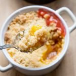 Een persoons bakje met daaruit geschept een lepel vol rabarber crumble en custard